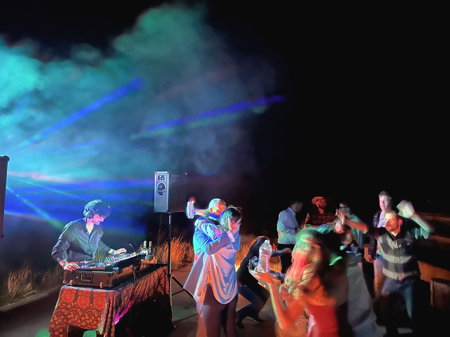 Guests dancing outdoors at night with colorful DJ lighting