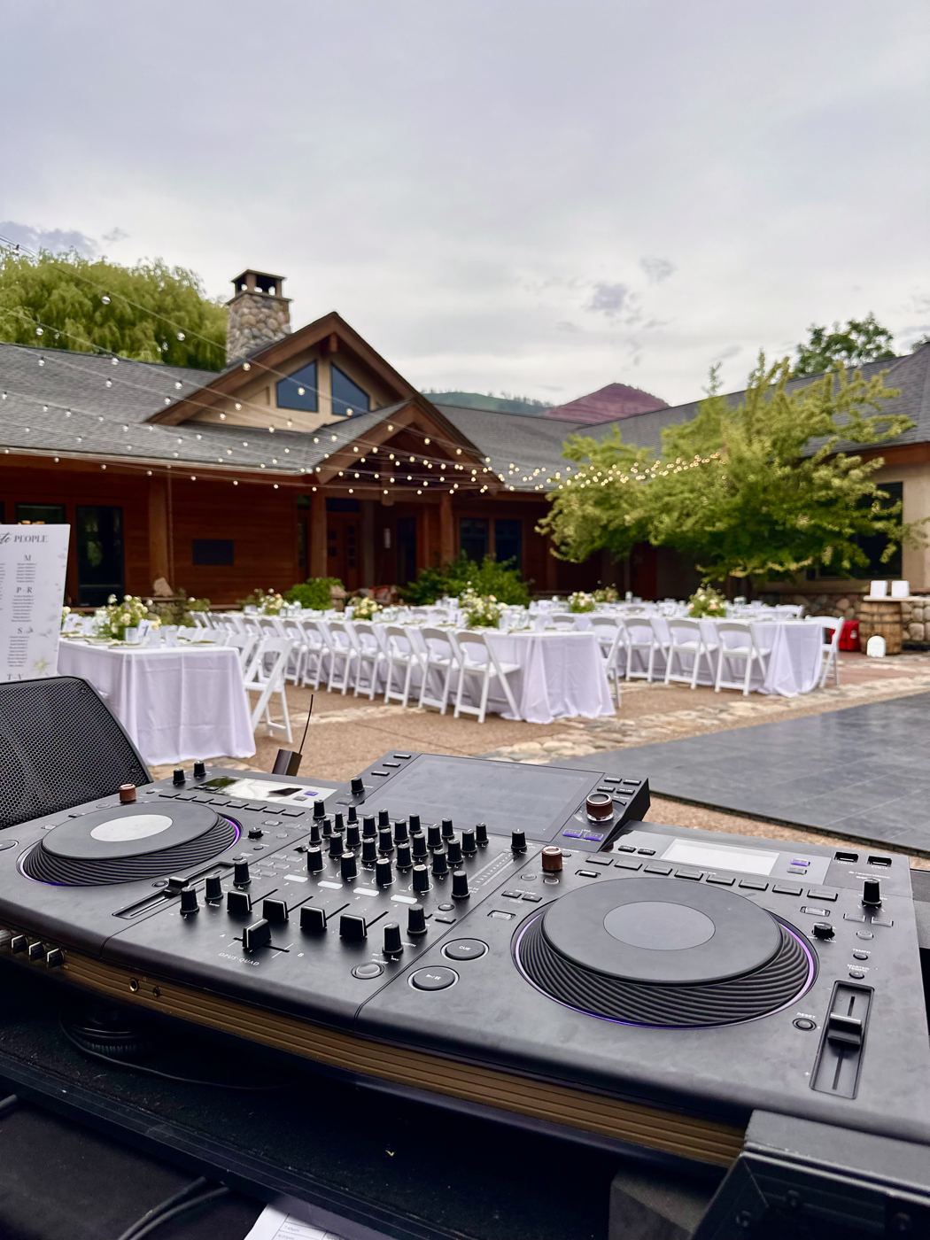 DJ decks overlooking an outdoor lodge courtyard reception with white tables