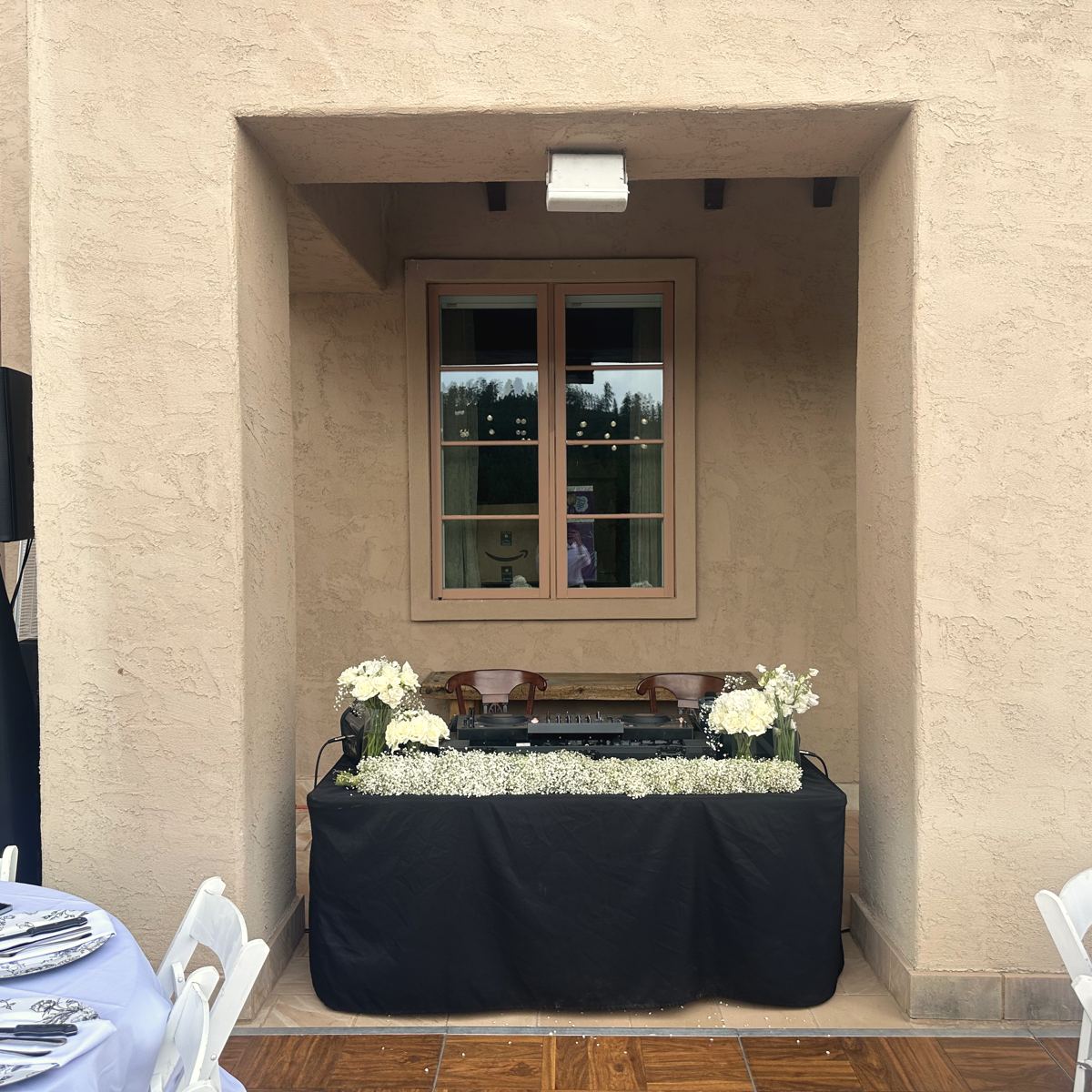 A DJ setup dressed with white florals between reception tables